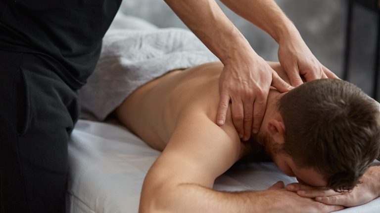Young handsome man enjoying a back massage. Professional massage therapist is treating a male patient in apartment. Relaxation, beauty, body and face treatment concept. Home massage.